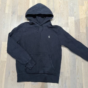 Ralph Lauren hoodie - Svart hoodie från Polo Ralph Lauren med klassisk broderad logga på bröstet. Tröjan har huva med snörning, känguruficka och långa ärmar. Tillverkad i mjuk bomull som är perfekt för kyliga dagar.
