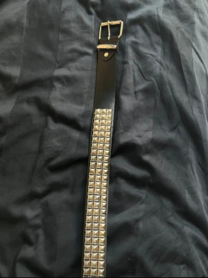 Nitbälte  - Säljer ett svart nitbälte i äkta läder. Köpt för ett par år sedan på EMP för ca 500kr. Nya hål har tagits för att passa mindre storlekar. Tecken på användning syns, främst på metalldelarna av spännet. Men fortfarande i gott skick. 