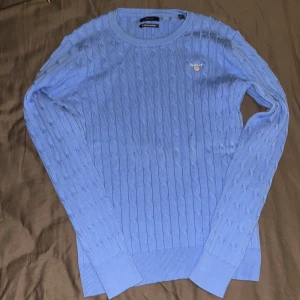 Blå kabelstickad tröja från GANT - Blå kabelstickad tröja från GANT med rund hals och diskret logga broderad på bröstet. Tröjan har långärmad passform och ribbade muddar vid ärmslut och nederkant. Perfekt för dig som gillar klassisk och stilren look. Finns ej prislapp, togs bort vid öppning. Varan är aldrig använd säljs då jag fick den i present men passar inte mig. Storlek är M fast ganska säker på att det passar S passformen är tajt. Normal pris är 1600kr säljs för 499 eftersom jag inte ser att den är värd 1600 i mina ögon. 