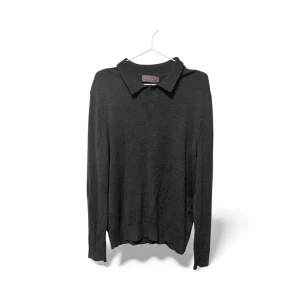 Svart pikétröja i merinoull från Morris - Klassisk svart pikétröja från Morris i 100% merinoull. Tröjan har lång ärm, krage och knappar framtill. Perfekt för dig som gillar stilrena och tidlösa plagg med mjuk och skön känsla. Passar dig som vill ha en enkel men snygg look.