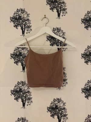 Brun croppad linnetopp från SHEIN - Säljer en brun croppad linnetopp från SHEIN i storlek XS. Toppen har tunna axelband och ärmlös design, perfekt för dig som gillar enkel och stilren look. Materialet är mjukt och lätt, vilket gör den skön att bära. Passformen är tight och toppen är enfärgad utan mönster.