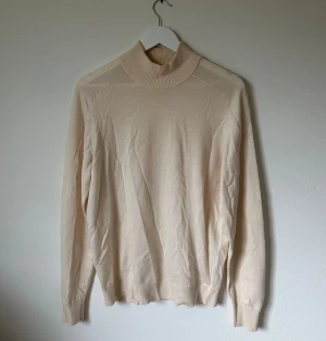 Beige polotröja från Uniqlo U - Snygg beige polotröja från Uniqlo U i storlek L. Tröjan har en hög ribbad krage och är tillverkad i mjuk bomull. Den har långärmad passform och ribbade muddar vid ärmslut och nederkant. Perfekt för lager-på-lager under hösten och vintern. 4Ä13