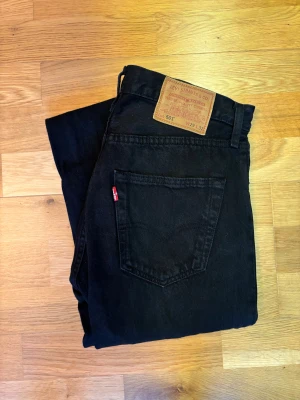 Svarta Levi's 501 jeans W29 L32 - Svarta Levi's 501 jeans med klassisk rak passform och fem fickor. Jeansen har en snygg läderpatch bak i midjan och den ikoniska röda Levi's-taggen på bakfickan. Tillverkade i slitstarkt jeanstyg med knappgylf och bälteshällor.