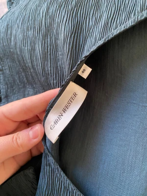 Mörkblå blus från Carin Wester - Säljer en mörkblå blus från Carin Wester med puffiga korta ärmar och volang nedtill. Blusen har en snygg struktur i tyget och ett band som kan knytas i ryggen. Perfekt för dig som gillar unika detaljer och stilren design.