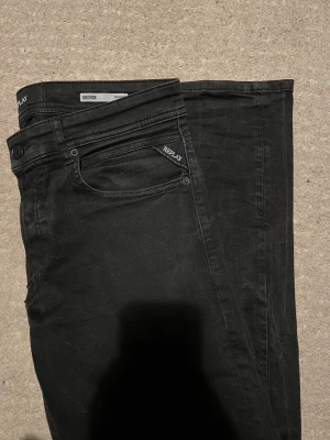 Replay Grover svarta jeans - Svarta Replay Grover jeans med klassisk femficksdesign och snygga detaljer på fickorna. Jeansen har rak passform och är tillverkade i mjukt jeansmaterial med en mörk ton. Perfekt för dig som gillar stilrena och tidlösa jeans.