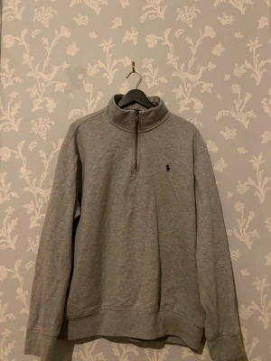 Grå half zip tröja Polo Ralph Lauren - Säljer en grå långärmad tröja från Polo Ralph Lauren i storlek XL. Tröjan har en stilren half zip-dragkedja vid halsen och klassisk logga broderad på bröstet. Tillverkad i mjuk bomull, perfekt för chill höst- och vinterdagar.