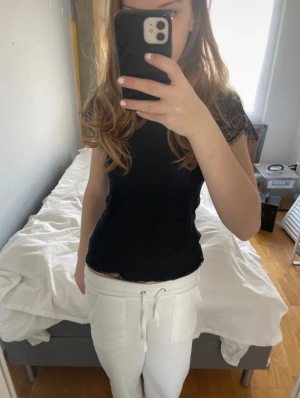 Svart spetsblus med kort ärm - Supersnygg svart blus i spets med korta ärmar och rund hals. Blusen har ett detaljerat spetsmönster och lätt transparenta ärmar som ger en cool och feminin vibe. Perfekt att styla med jeans eller kjol för en trendig look. (Ai)
