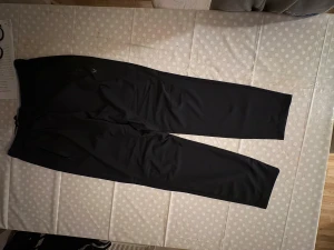 Svarta träningsbyxor från SOC - Svarta träningsbyxor från SOC med elastisk midja och snörning. Byxorna har raka ben och dragkedjeförsedda fickor. Perfekta för träning eller chill, tillverkade i ett mjukt och stretchigt syntetmaterial.