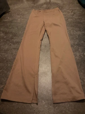 Beige vida leggings med slits - Säljer ett par beige leggings med utsvängda ben och slits framtill. Mjukt och stretchigt material som sitter skönt på kroppen. Perfekta för en avslappnad och trendig look.