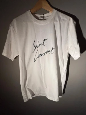 Saint Laurent T-shirt - Jag säljer denna riktigt eftertraktade Saint Laurent T-shirt som är perfekt för sommaren! Den är Storleken M! Helt nytt skick! Nypris runt ca 2000 kr! Kontakta mig vid funderingar.