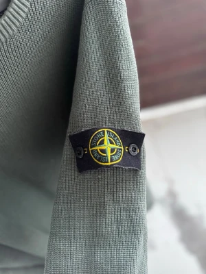 Grön stickad tröja från Stone Island - Snygg grön stickad tröja från Stone Island med klassisk patch på ärmen. Tröjan har rund halsringning och ribbade muddar. Perfekt för dig som gillar streetwear och vill ha något stilrent men ändå unikt.