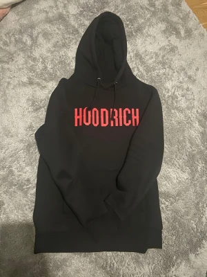 Hoodrich hoodie - Svart Hoodrich med stor röd logga framtill. Mjuk, bekväm och passar perfekt för vardagen och allt annat! Inte så använd alls, och för ett magiskt pris!