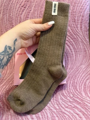 Bruna ribbade strumpor från Miu Miu - Snygga bruna ribbade strumpor från Miu Miu med diskret logotyp på skaftet. Perfekta för dig som vill ha en stilren och trendig look. Strumporna är stickade och känns både mjuka och bekväma.