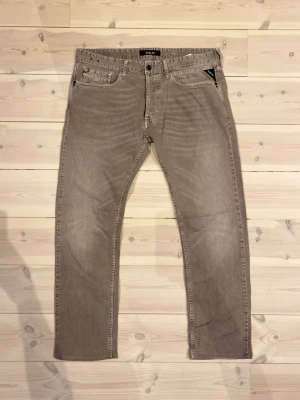 Replay jeans  - Snygga beige jeans från Tiger of Sweden med raka ben och klassisk femficksmodell. Jeansen har diskreta slitningar och tydliga sömmar, samt en svart patch med logga bak i midjan. Perfekta för en stilren och avslappnad look.