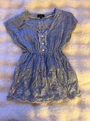 Blåvit randig blus från KRISS - Söt blåvit lång blus med ränder och broderade blommor. Klänningen har v-ringning, knappar framtill och spetsdetaljer. Tillverkad i bomull och har korta ärmar. Perfekt för sommarens varma dagar. I storlek S💕💕