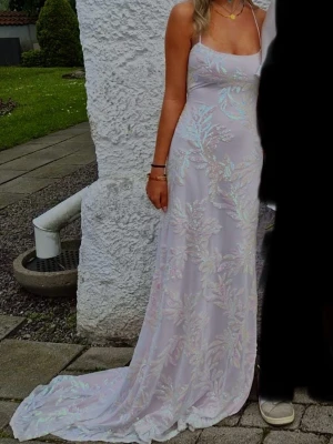 Balklänning  - Säljer en elegant långklänning i ljus rosa ish färg med glittriga detaljer och mönster. Klänningen har smala axelband och figurnära passform, perfekt för speciella tillfällen. Materialet ger en skimrande effekt och känns lyxigt.