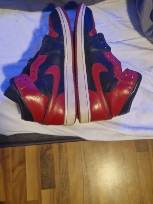 Nike Air Jordan 1 svart/röd sneakers - Säljer ett par klassiska Nike Air Jordan 1 sneakers i svart och rött skinn med vita sulor. Ikonisk high-top modell med röda detaljer och Swoosh-logga på sidan. Perfekta för dig som gillar streetwear och vill sticka ut med en tidlös sneaker.