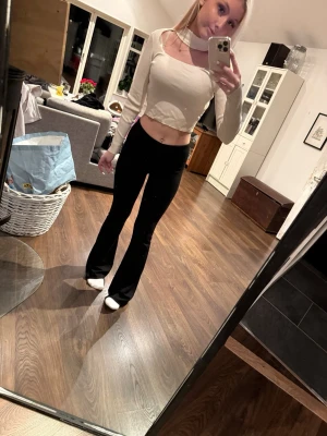 Ljusbeige croppad ribbad topp - Trendig ljusbeige croppad topp med lång ärm och fyrkantig ringning. Toppen är ribbad och har en unik choker-detalj runt halsen. Perfekt för dig som gillar stilrena och moderna plagg.