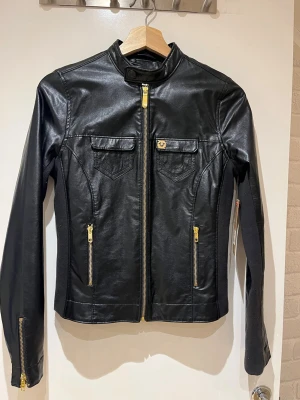 True Religion - svart skinnjacka med gulddetaljer - Snygg svart skinnjacka i äkta läder från True Religion med guldfärgade dragkedjor och detaljer. Jackan är helt oanvänd och prislappen är på. Säljes då jag fått den i present från USA men den var för liten. 