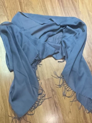 Ljusblå sjal med fransar - En stilren ljusblå sjal med tunna fransar längs kanterna. Sjalen är rektangulär och tillverkad i ett mjukt, tunt tyg som ger en skön känsla. Perfekt att svepa runt halsen eller axlarna för en extra touch till din outfit.