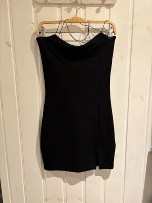 Svart crossbands kortklänning NA-KD - Stilren svart kortklänning med smala axelband och liten slits framtill. Klänningen har en figurnära passform och en enkel, elegant design. Står M i klänningen men passar S