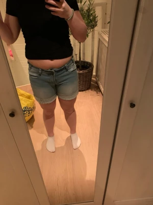 Ljusblå jeansshorts med uppvik - Säljer ett par ljusblå jeansshorts med klassisk femficksmodell och snygga uppvikta benslut. Shortsen har normalhög/låg midja och stängs med dragkedja och knapp. Perfekta för sommaren och lätta att matcha med olika toppar. Säljer pågrund av att det inte riktigt är min stil