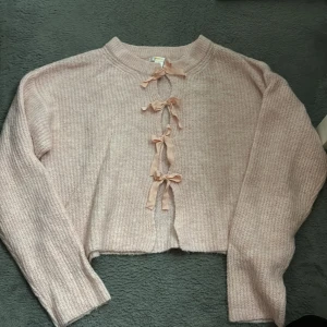 Ljusrosa stickad tröja med rosetter - Supersöt ljusrosa stickad tröja från Gina Tricot med 4 dekorativa rosetter framtill. Tröjan har lång ärm, ribbad.