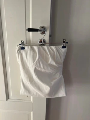 Vit tubtopp från Zara  - Säljer en vit axelbandslös topp i omlottstil med lätt drapering framtill. Köpt på Zara men säljer då den är för liten för mig. Passar dig som gillar minimalistiskt mode och vill ha något enkelt men snyggt.❤️❤️aldrig använd 