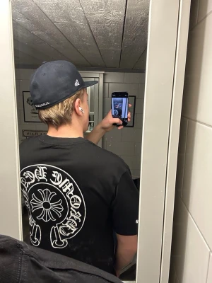 Svart Chrome Hearts t-shirt - Säljer en svart t-shirt från Chrome Hearts med stort vitt tryck på ryggen och logga på ärmen. T-shirten har rund hals och korta ärmar. Materialet känns som mjuk bomull och passformen är normal. Perfekt för dig som gillar streetwear och vill sticka ut.