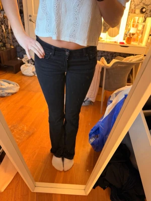 Svarta bootcut jeans med låg midja - Säljer ett par svarta bootcut jeans med låg midja och klassisk femficksdesign. Jeansen har en smal passform upptill och lätt utsvängda ben. Perfekta till en avslappnad och trendig look. Materialet är denim i bomull med lite stretch.
