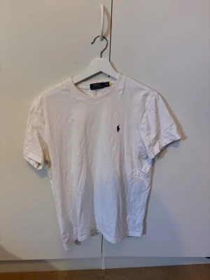 Vit t-shirt från Polo Ralph Lauren - Klassisk vit t-shirt från Polo Ralph Lauren med rund hals och korta ärmar. T-shirten har den ikoniska lilla broderade loggan på bröstet och är tillverkad i mjuk bomull för en skön känsla. Perfekt basplagg till garderoben.