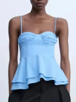 Ljusblå topp från Zara💗💗 - Supersöt ljusblå topp med smala axelband och volang nertill. Toppen har en söt rynkad detalj vid bysten och en peplum-liknande form som ger en feminin siluett. Perfekt för varma dagar och snygg att styla med både jeans och kjol.