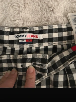 Rutiga jeans från Tommy Jeans - Säljer ett par svartvita rutiga jeans från Tommy Jeans. De har klassiskt femficksmodell, bälteshällor och detaljer med Tommy Jeans-logga. Materialet är mjukt och följsamt, perfekt för dig som vill sticka ut med ett coolt mönster.