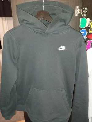 Svart Nike hoodie - Snygg svart hoodie från Nike med klassisk vit logga på bröstet. Hoodien har huva och en stor magficka framtill. Tilllverkad i mjukt och bekvämt material som passar året runt. Bra skick storlek 158 170cm