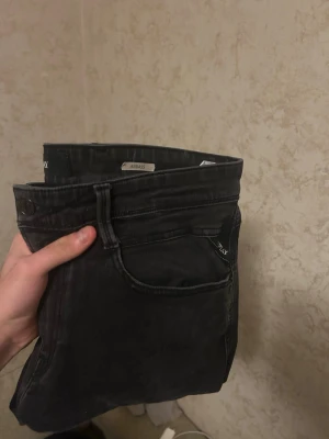 Svarta slim fit jeans Replay - Säljer ett par svarta slim fit jeans från Replay, modell Anbass. Jeansen har klassisk femficksdesign, låg midja och smal passform. Perfekta för dig som gillar en stilren och modern look.