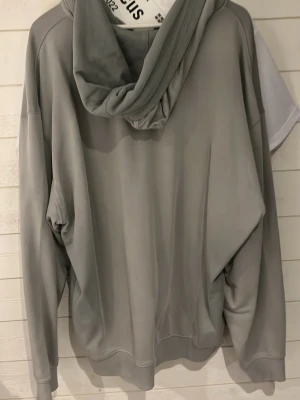 Grå zip-hoodie med fickor - Snygg grå hoodie med dragkedja framtill och stora kängurufickor. Modellen har huva med dragsko och ribbade muddar vid ärmslut och nederkant. Perfekt för en avslappnad och stilren look.