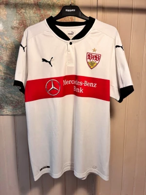 VFB Stuttgart Puma 2017/18 home shirt, storlek XL - Mycket gott skick.  #stuttgart #vfbstuttgart #bundesliga #puma #germany #pavard #gomez #badstuber   Vit VfB Stuttgart fotbollströja med röd rand över bröstet och Mercedes-Benz Bank tryck. Puma loggan syns på höger bröst och klubbmärket på vänster. Tröjan har en svart krage och svarta detaljer på ärmarna. Årtalet 1893 är tryckt på baksidan av nacken.