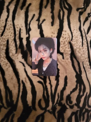 Fotokort Felix Stray Kids - Säljer ett fotokort med Felix från Stray Kids, rektangulär form och blanka yta. Kortet har en färgglad bakgrund och visar en person med svart hår, smycken och svart outfit. Perfekt för samlare av K-pop eller idolmerch.