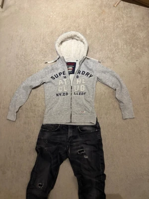 Zip-hoodie från Superdry - Säljer denna extremt stilrena hoodie från superdry. Väldigt mjuk och skönt material i luvan och perfekt att ha nu i kallare tider. Det sår storlek M men den är storlek S skulle jag säga. S/XS