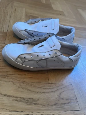 Vita Philippe Model sneakers - Stilrena vita sneakers från Philippe Model med lågt skaft och klassisk design. Skorna är gjorda i läder med detaljer i grått och har en svart sula med tydlig logotyp undertill. Perfekta för dig som gillar minimalistisk och clean stil. 📦köp så skickar jag nästa dag eller samma dag snabba leveranser. 💨