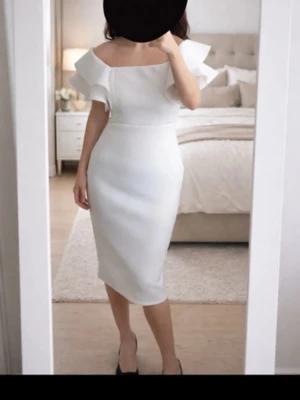 Vit offshoulder klänning med volang - Elegant vit klänning med offshoulder och volangdetaljer upptill. Klänningen är figurnära och har en midilång passform som ger en stilren siluett. Perfekt för dig som vill ha en klassisk och chic look. Endast använd 1 gång