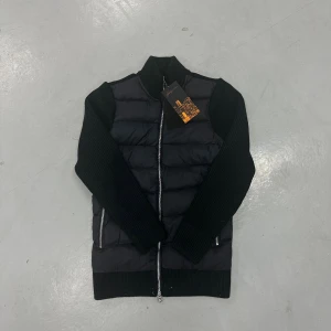 Marcel true classic cardigan frånLeon Marcel  - Svart cardigan från Leon Marcel. Jackan har quiltad framsida och stickade ärmar samt rygg i grov ribbad struktur. Två sidofickor med dragkedja och hel dragkedja framtill. Snygg, modern look med hög krage.