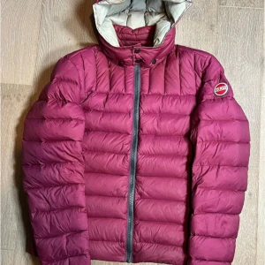 Vinröd dunjacka från Colmar - Säljer en vinröd dunjacka från Colmar med huva och dragkedja framtill. Snabbast frakt är tre dagar pga. detta är en förbeställning. Jackan har ett quiltat mönster och en badge med Colmar-loggan på ärmen. Perfekt för kalla dagar och riktigt snygg färg som sticker ut. Storlek M/50. Skriv om frågor uppstår, pris kan alltid diskuteras.