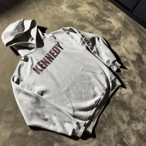 Vintage KENNEDY EAGLES Hoodie🇺🇸🦅 - Grå Vintage hoodie från Jerzees med tryck 'KENNEDY' på bröstet och ”EAGLES” längs ena ärmen. Klassisk känguruficka framtill och huva. Mjuk insida och relaxed fit, perfekt för chill dagar. Materialet är en blandning av bomull och polyester.