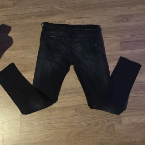Svarta Replay jeans, storlek 30/34 - Säljer ett par svarta Replay jeans i storlek 30. Jeansen har klassisk femficksdesign, snygga slitningar och raka ben. Materialet är stretchigt jeans och passformen är normal. Perfekta för dig som gillar stilrena och bekväma jeans.