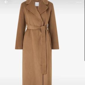 Klassisk beige kappa med bälte - Snygg lång beige kappa med breda slag och knytbälte i midjan. Stilren design med rak passform och långa ärmar, perfekt för dig som gillar en clean och tidlös look. Materialet är mjukt och ger en lyxig känsla.