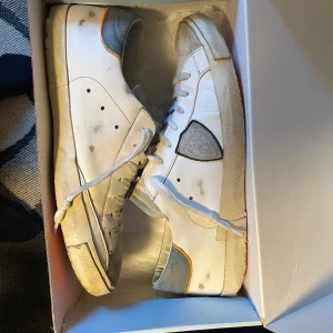 Vita sneakers från Philippe Model - Säljer ett par vita Philippe Model sneakers med grå och blå detaljer. Slitningar vid hälen, men inget man ser eller känner, skick 7/10. Boxen och tags medföljer, och priset är inte skrivet i sten, så kom gärna med prisförslag! 