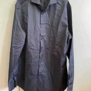 Svart skjorta Selected Homme XL /NY - Slim fit svart skjorta från Selected Homme i storlek XL. Skjortan har klassisk krage, knappar framtill och långa ärmar med manschett. Materialet är bomull och är lätt att stryka. Perfekt för dig som gillar stilrena och enkla plagg.