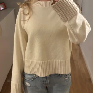 Beige stickad tröja med ribbade detaljer - Snygg vit stickad tröja med breda ribbade muddar vid ärmslut och nederkant. Tröjan har en rund halsringning och långärmade, lite loose passform. 