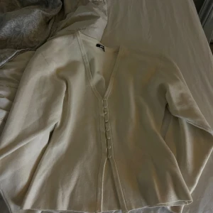 Beige kofta med v-ringning och knappar - Säljer en beige kofta från Only med snygg v-ringning och dekorativa knappar framtill. Koftan har långärmad design och är tillverkad i mjukt material som känns skönt mot huden. Perfekt för dig som gillar stilrena och enkla plagg.